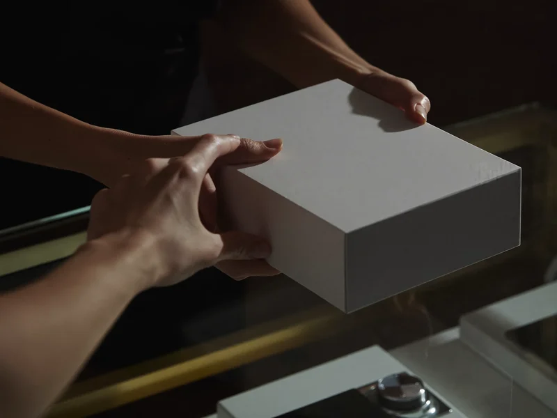 Mains tendant un téléphone en boîte neutre à un client par-dessus un comptoir vitré